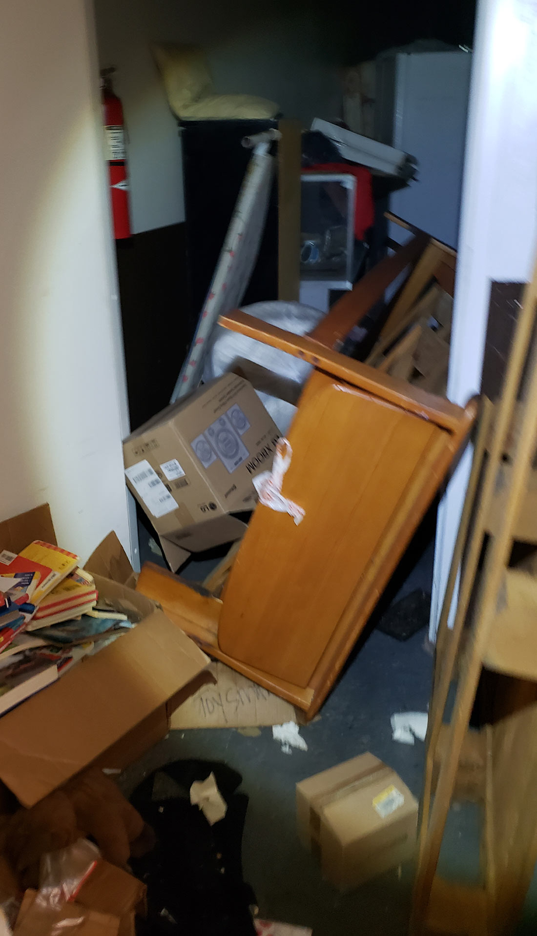 a doorway is blocked with disarrayed objects including furniture, packed boxes, wooden pallets and other debris