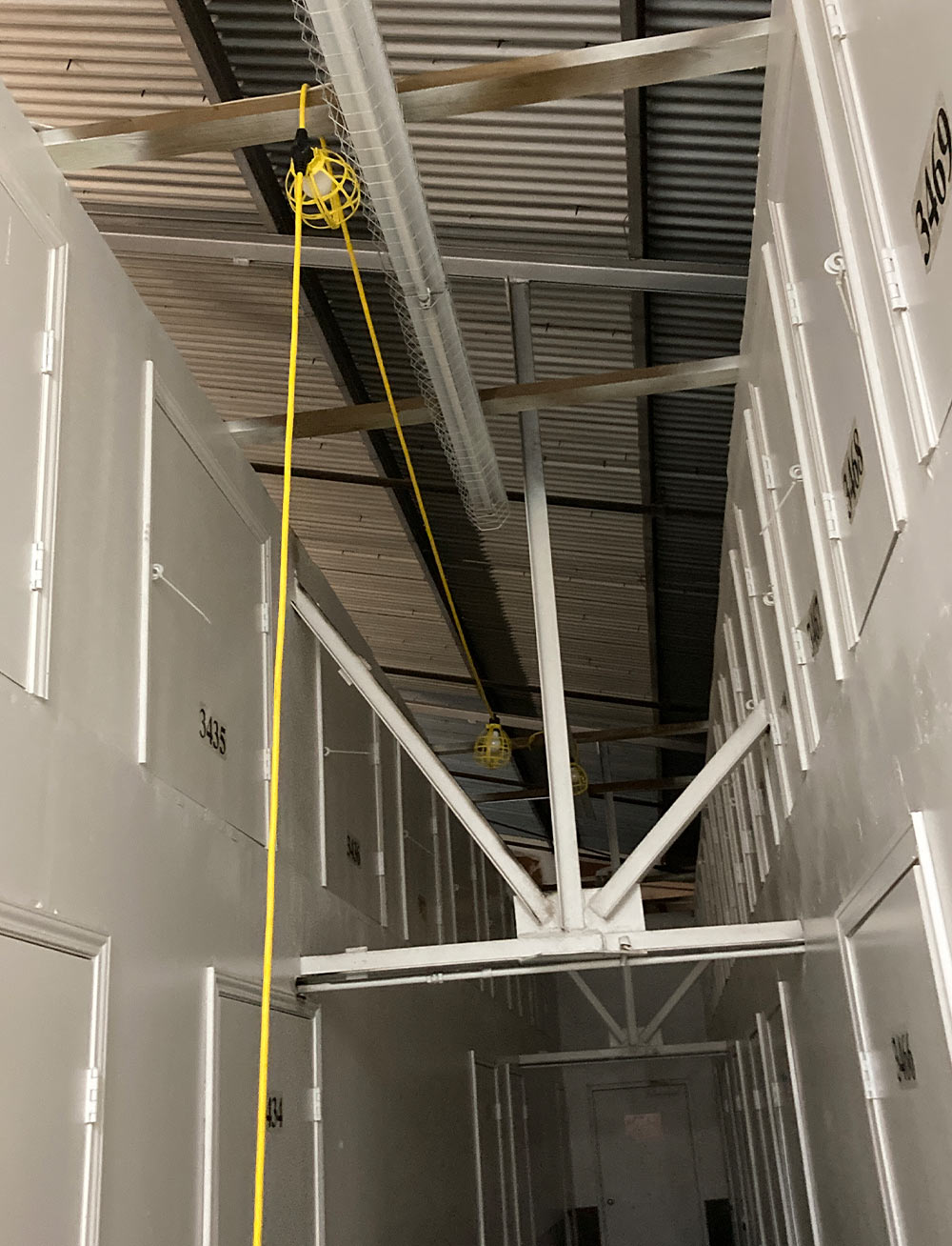 view upward toward the ceiling of the large storage facility hallway showing sparsely spaced drop-lights connected by extension cords