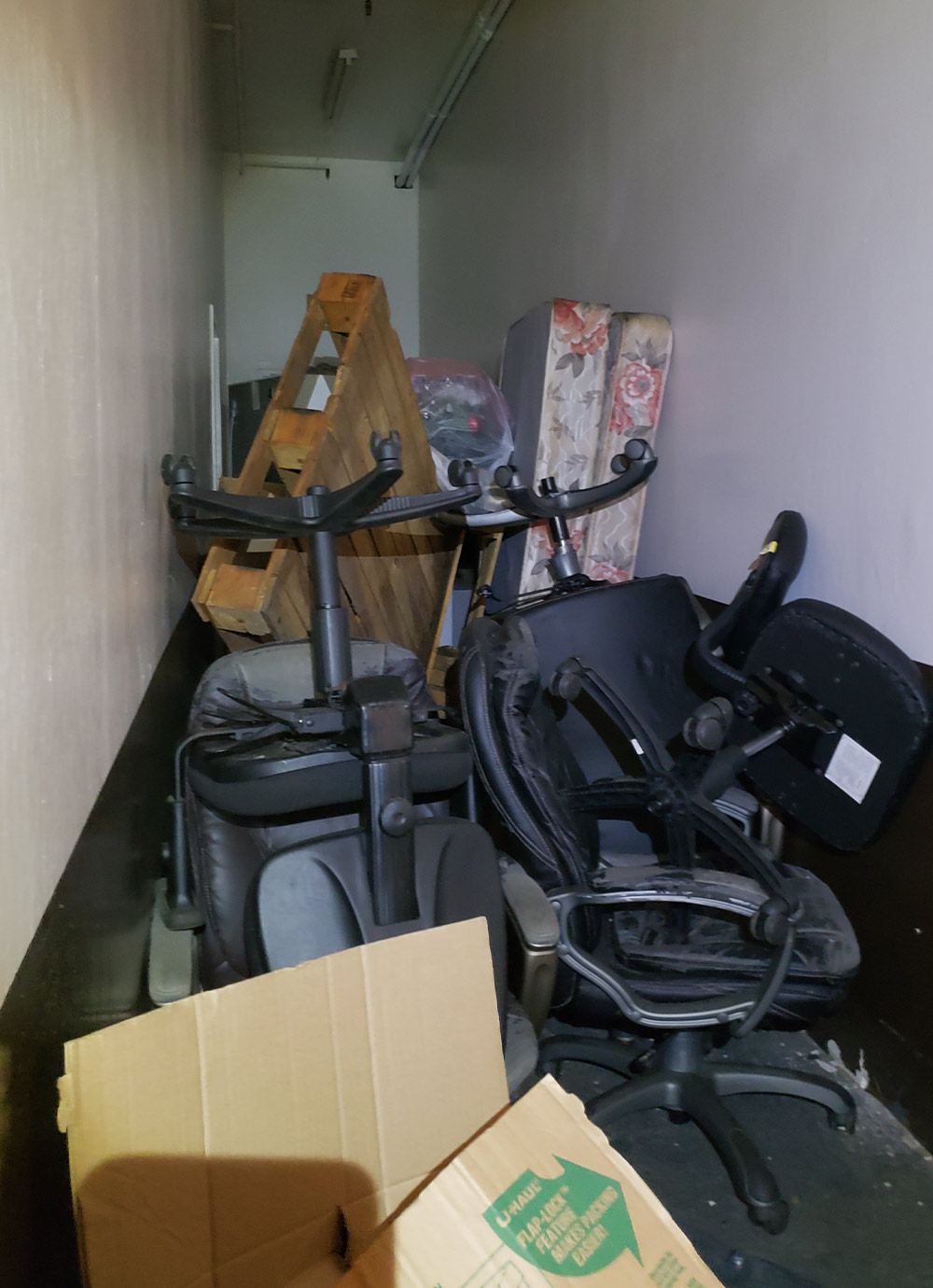 a hallway is jammed with various items including tattered rolling computer chairs, mattresses and wood pallets