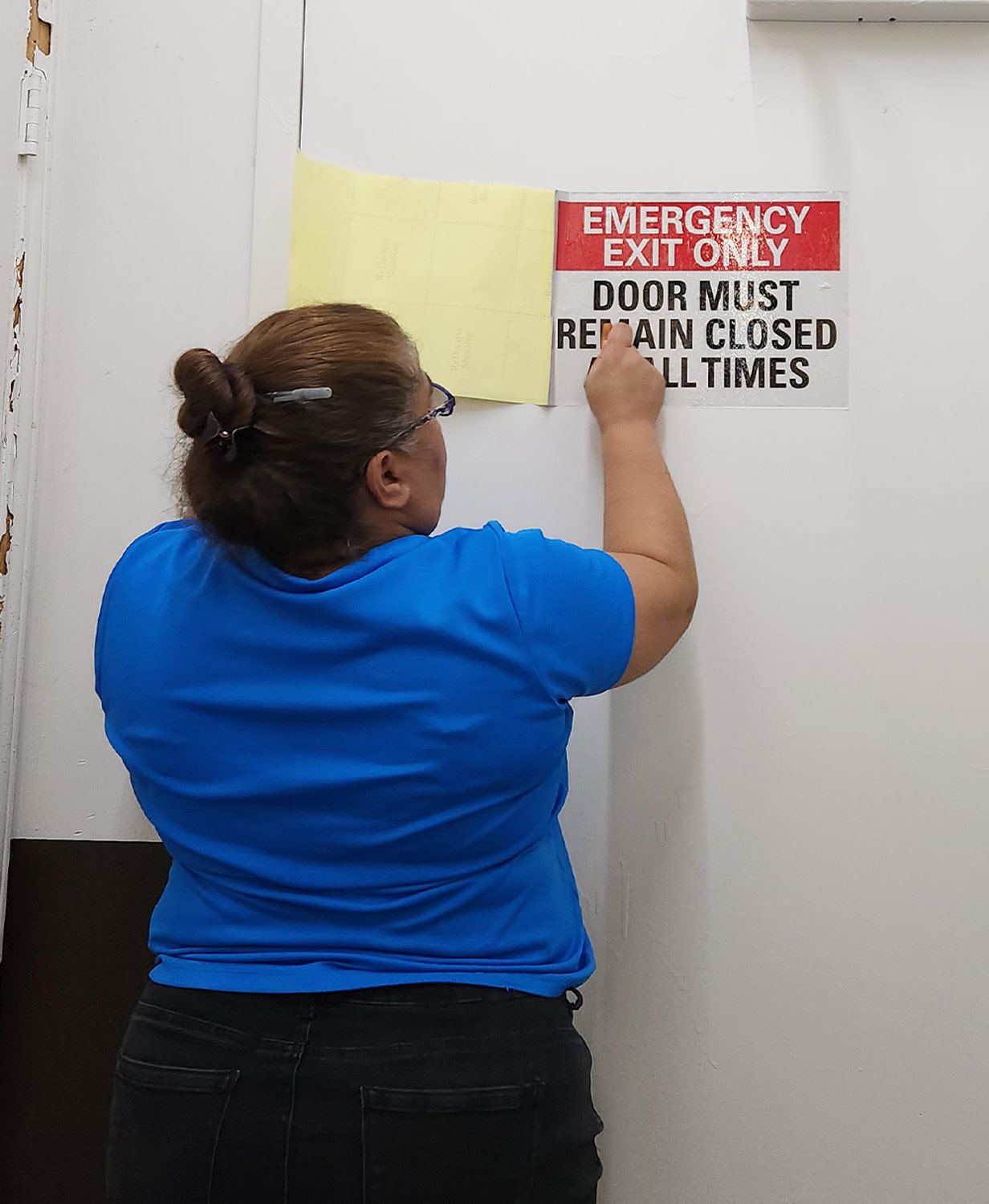 Jenny Rodrigues applies an Emergency Exit Only sign to a door