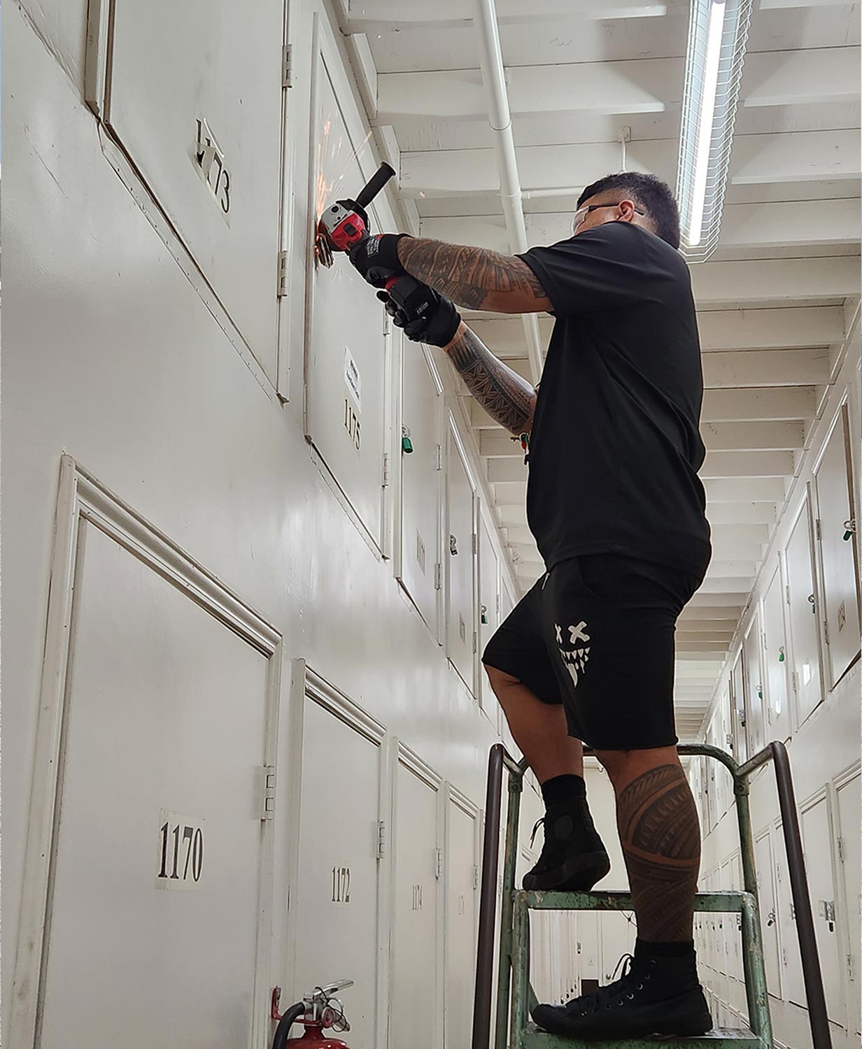 a man on a ladder uses a grinder to cut a padlock from a higher storage compartment