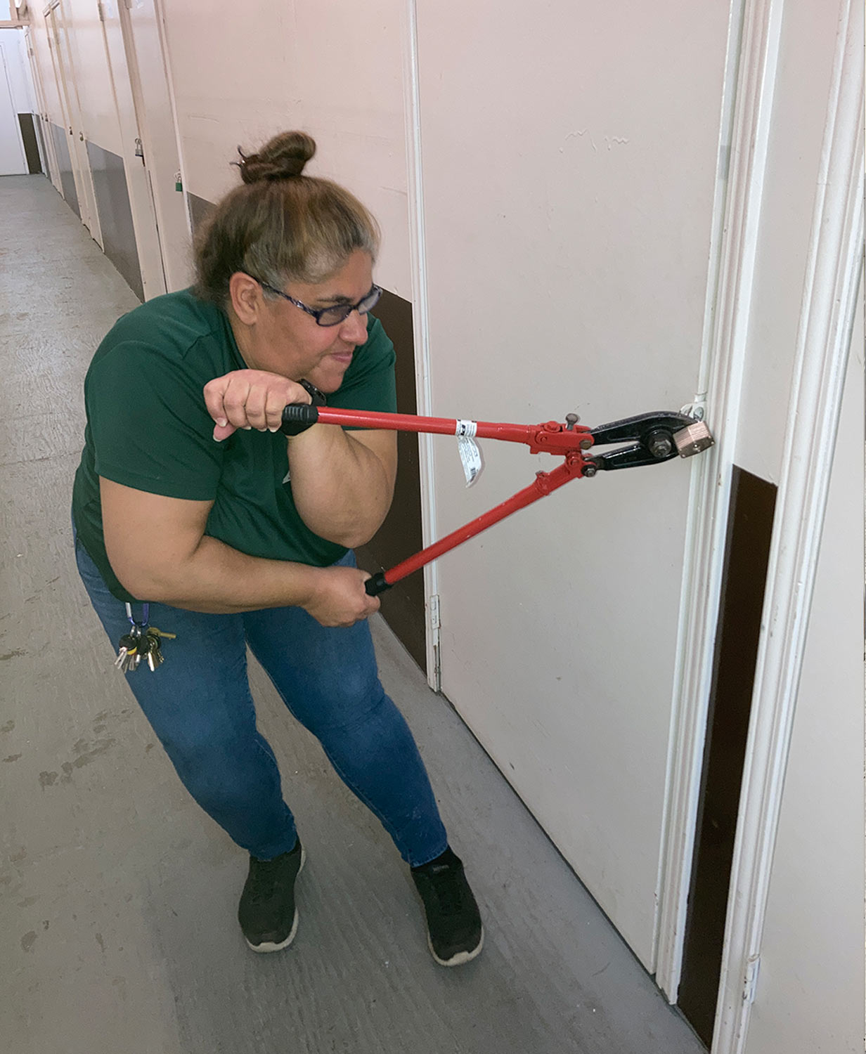 Jenny Rodrigues squinches her face while using her strength to break a lock on a storage door