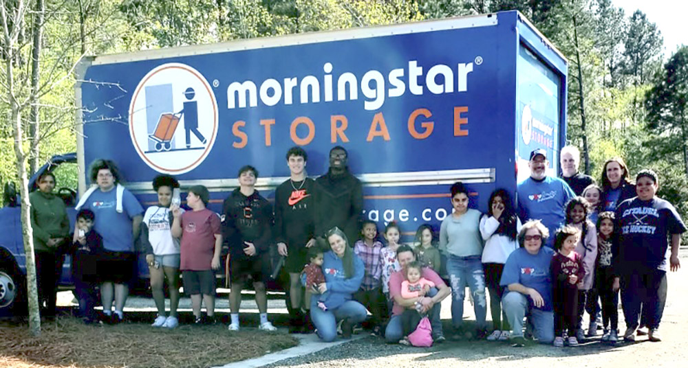 Group of individuals posing outside on the side of the Morningstar Storage truck on a sunny day