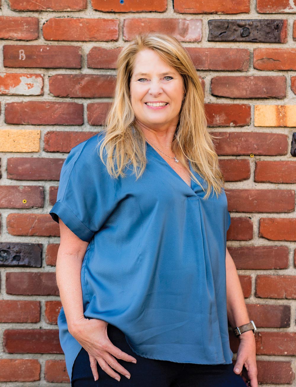 Pam Domingue smiling for a photo in front of a brick wall