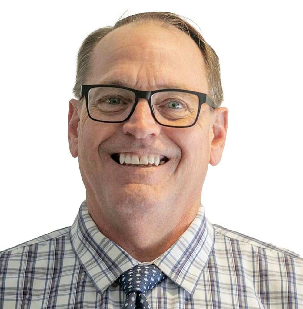 Portrait headshot photograph of Ron Pell smiling in a multi-colored striped button-up dress shirt (blue/purple/grey) and multi-colored pattern tie (blue/white)