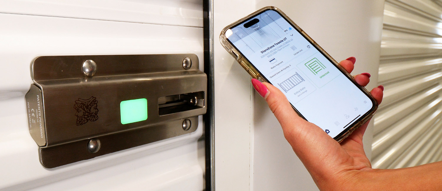 close view of the LED lighted fingerprint lock on a storage door and a woman's hand that holds a smartphone displaying the StoreEase tenant mobile interface