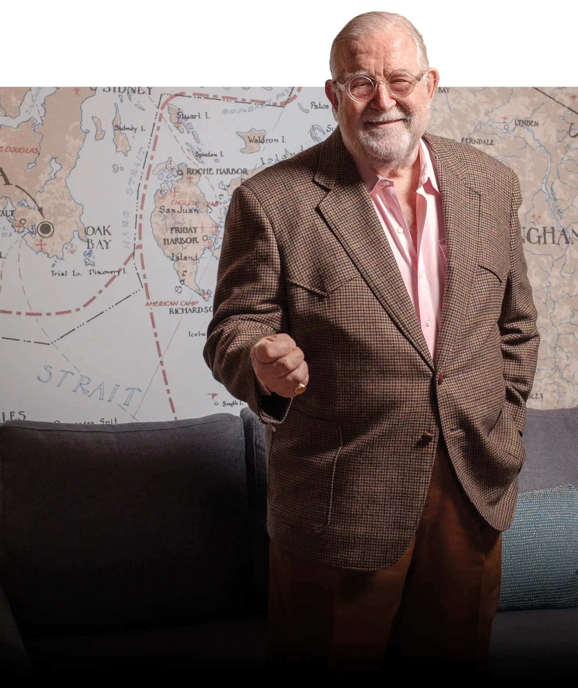 Hardy Good in brown suit smiling in front of large map and blue couch