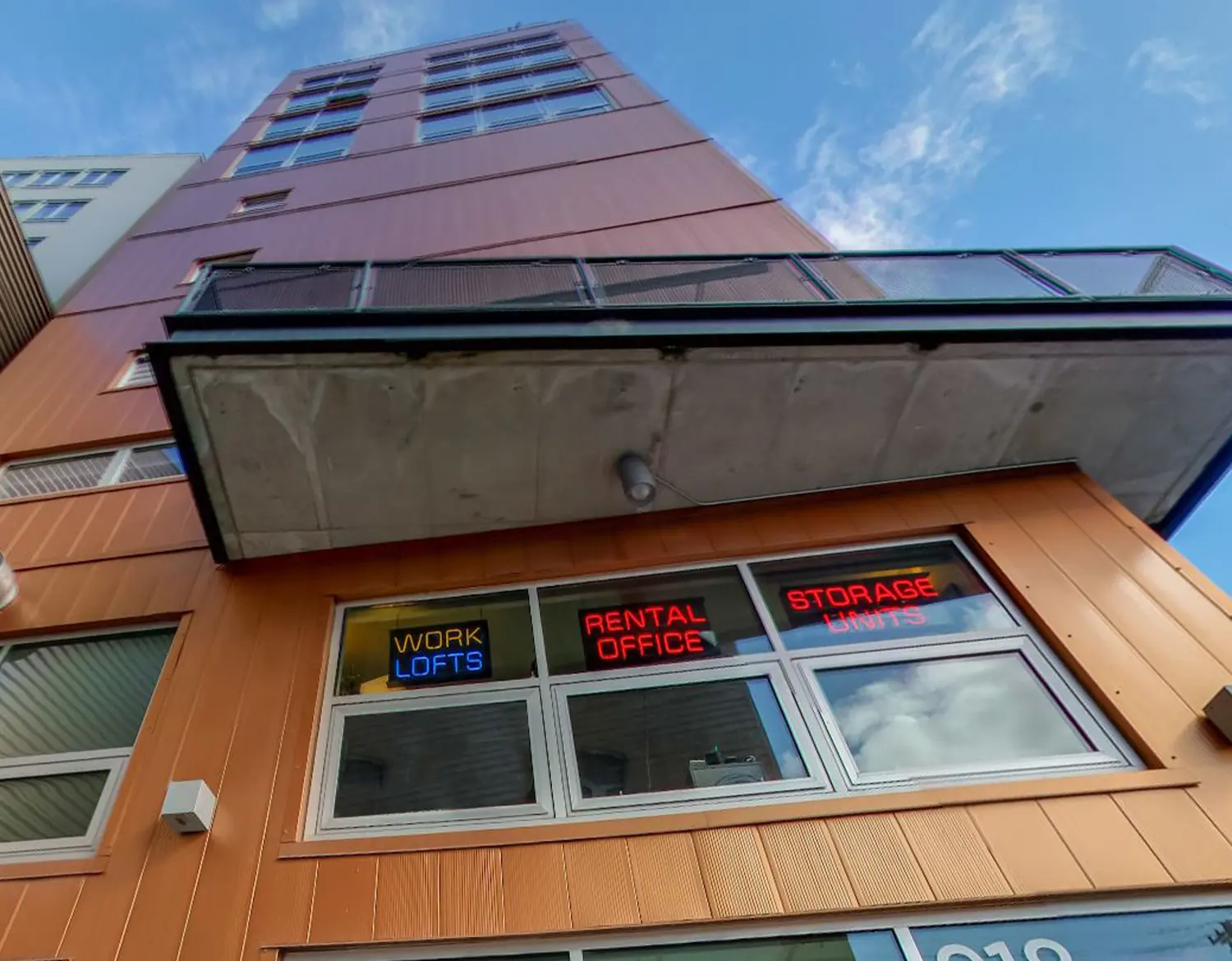 close view of the neon signs that read Work Lofts, Rental Office and Storage Units in the second floor window of a multi-storied storage facility