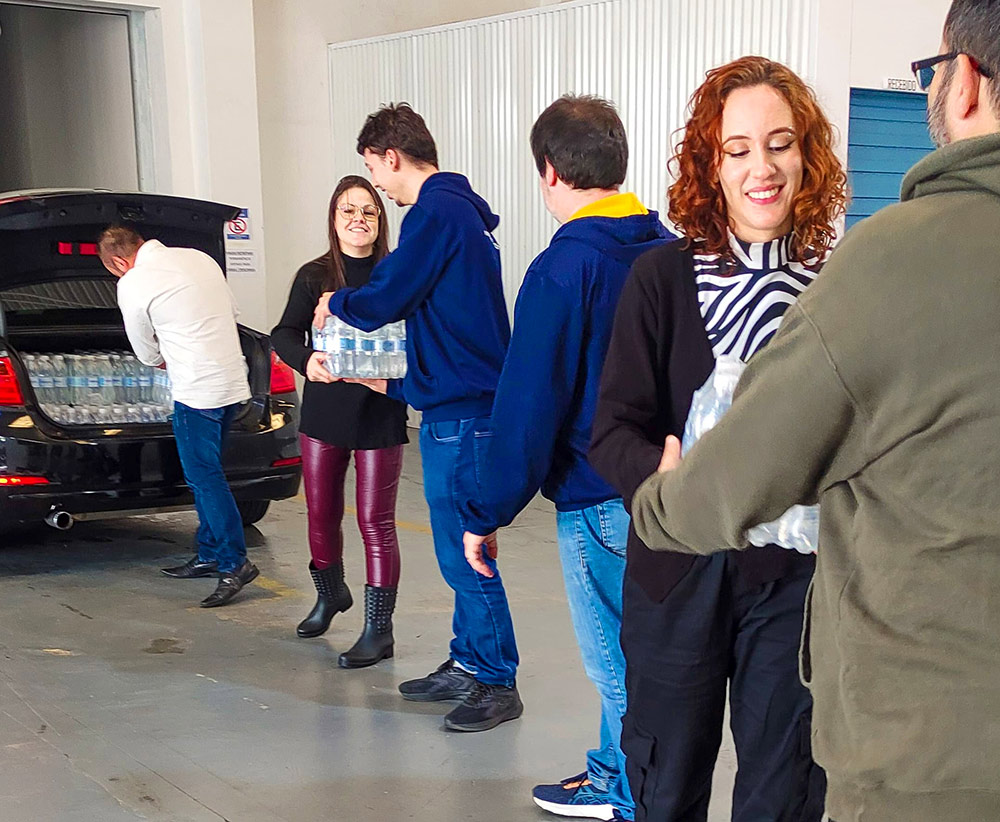 A group of people forming a line exchanging bottles of water from the trunk filled with water for distribution