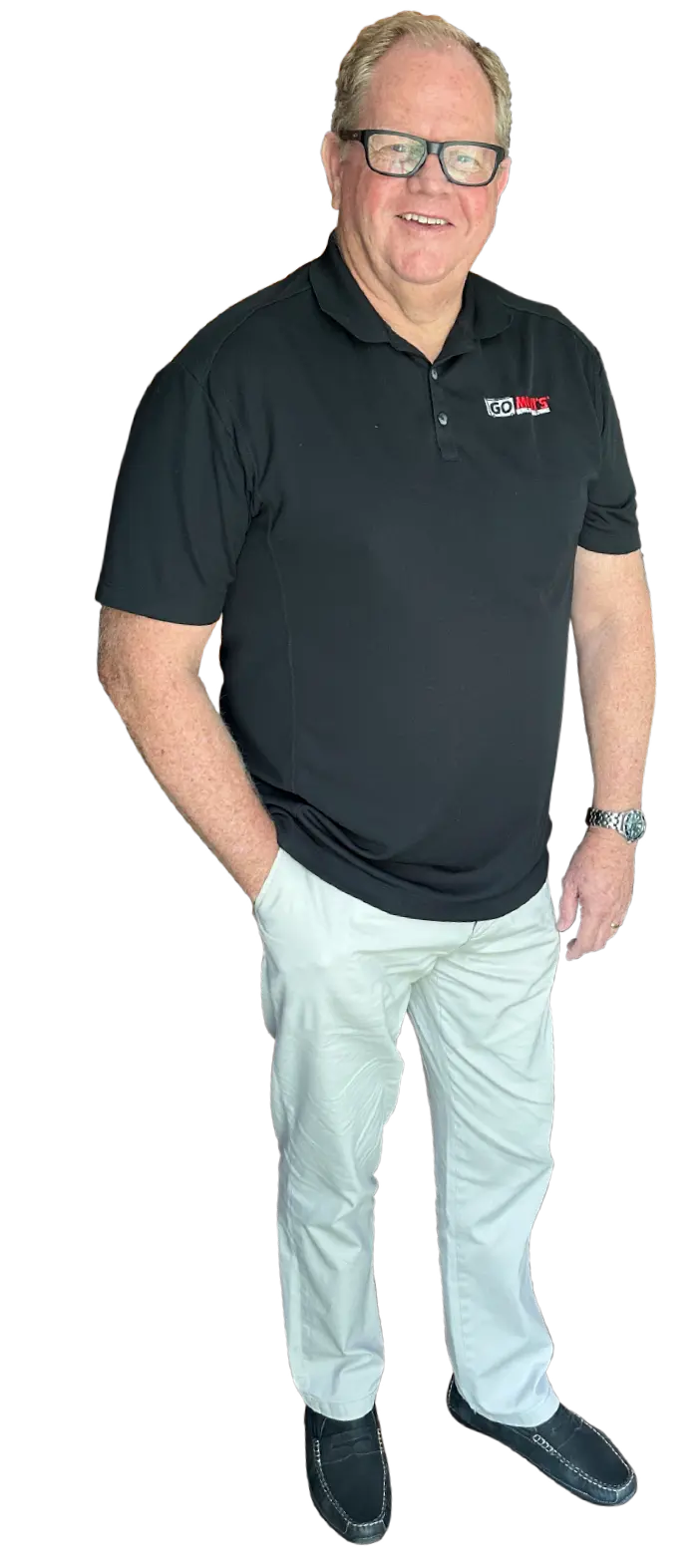 Portrait photograph of Chris Walls standing and smiling in a black Go Mini's company branded white/black/red logo polo top shirt as he has his right hand casually resting in his right off-white colored chino jean pocket; he also has on black/white trim colored work loafer shoes