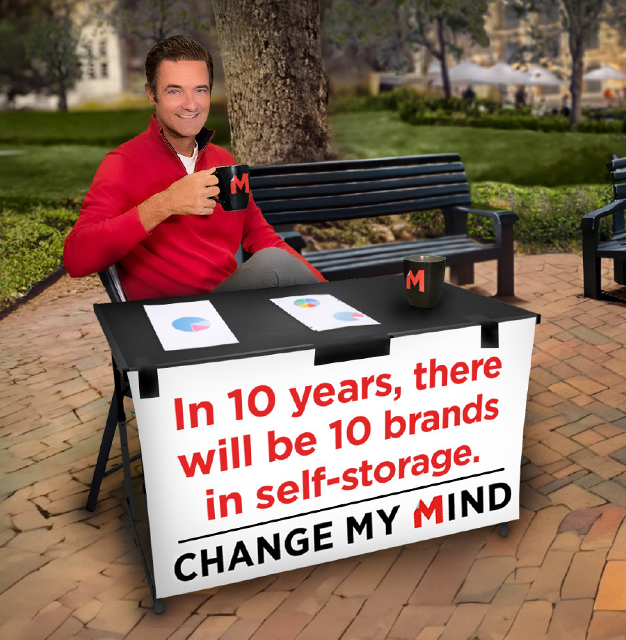 man sitting at table with sign stating "In 10 years, there will be 10 brands in self-storage. Change my mind."