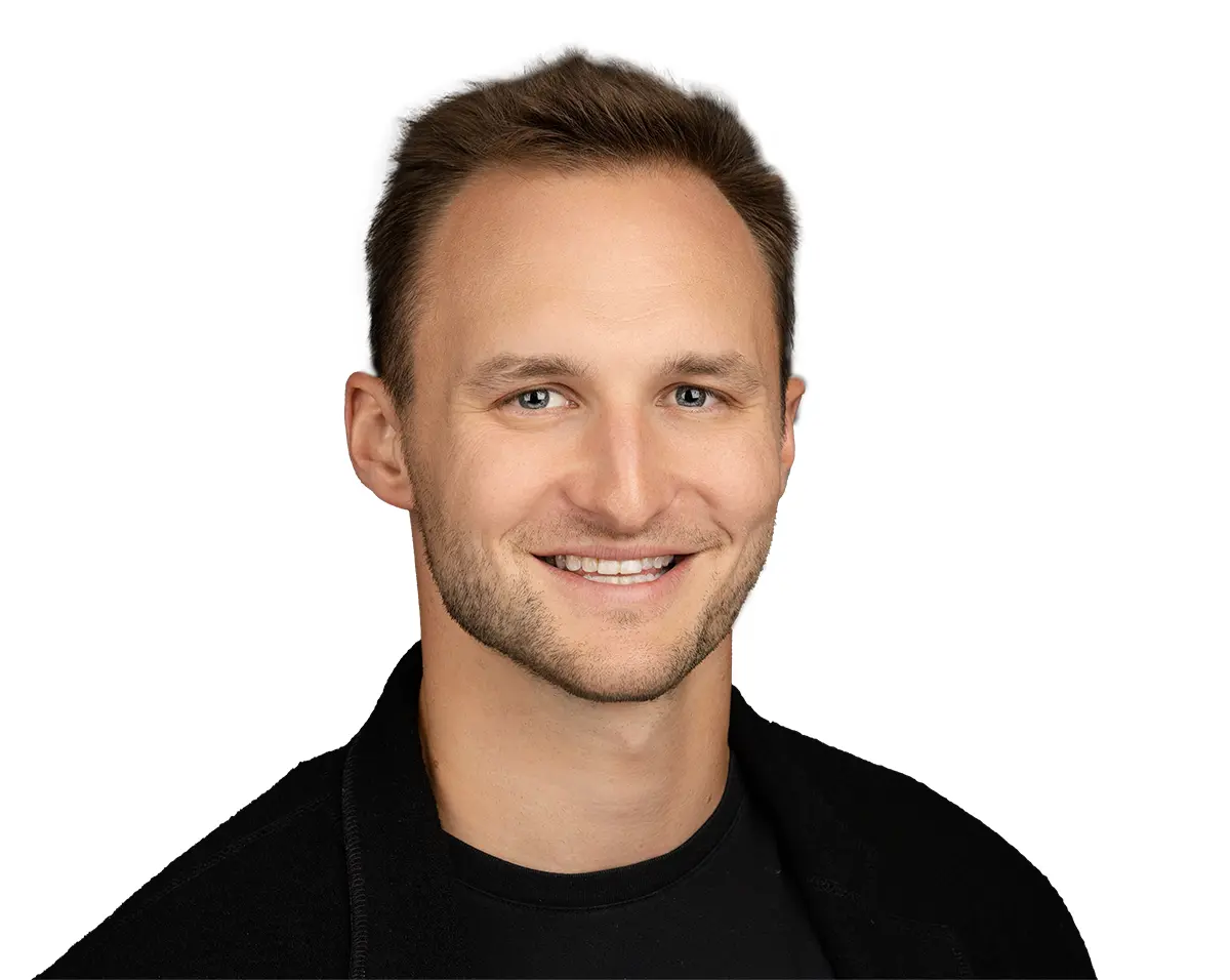 Portrait headshot photograph of Jacob Pandl smiling in a black open coat jacket and black t-shirt underneath