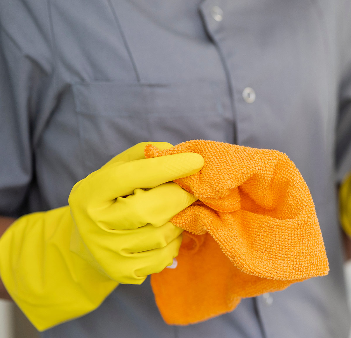 close cropped view of a yellow gloved hand holding a bright orange microfiber towel