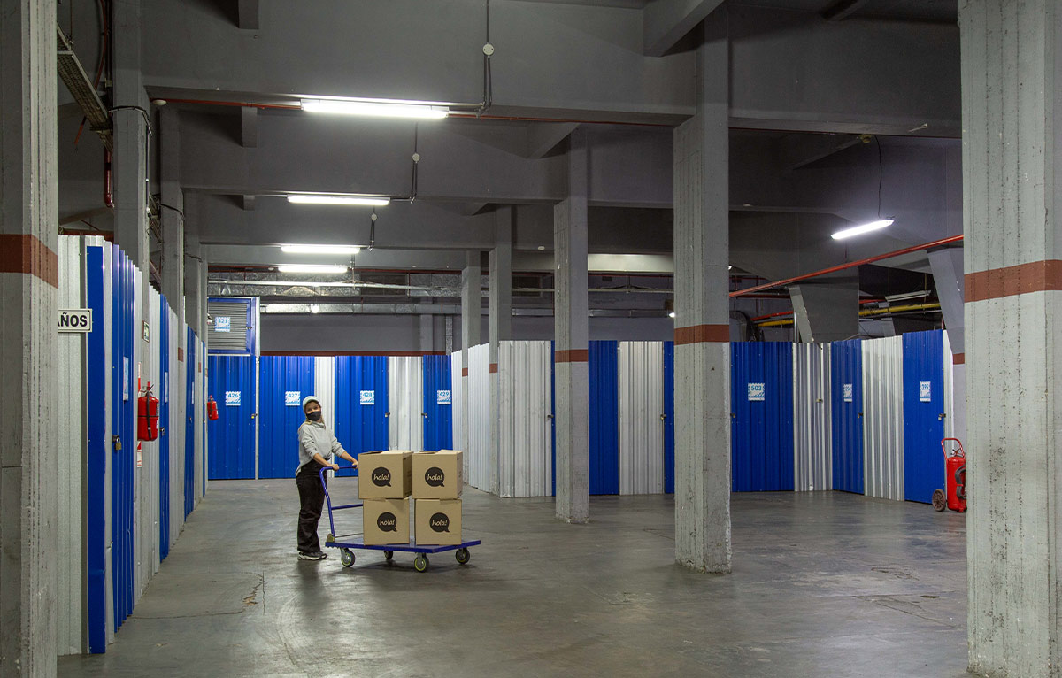 wide view of a woman pushing a stacked cart in a large open plan room, its walls lined with storage units with blue doors