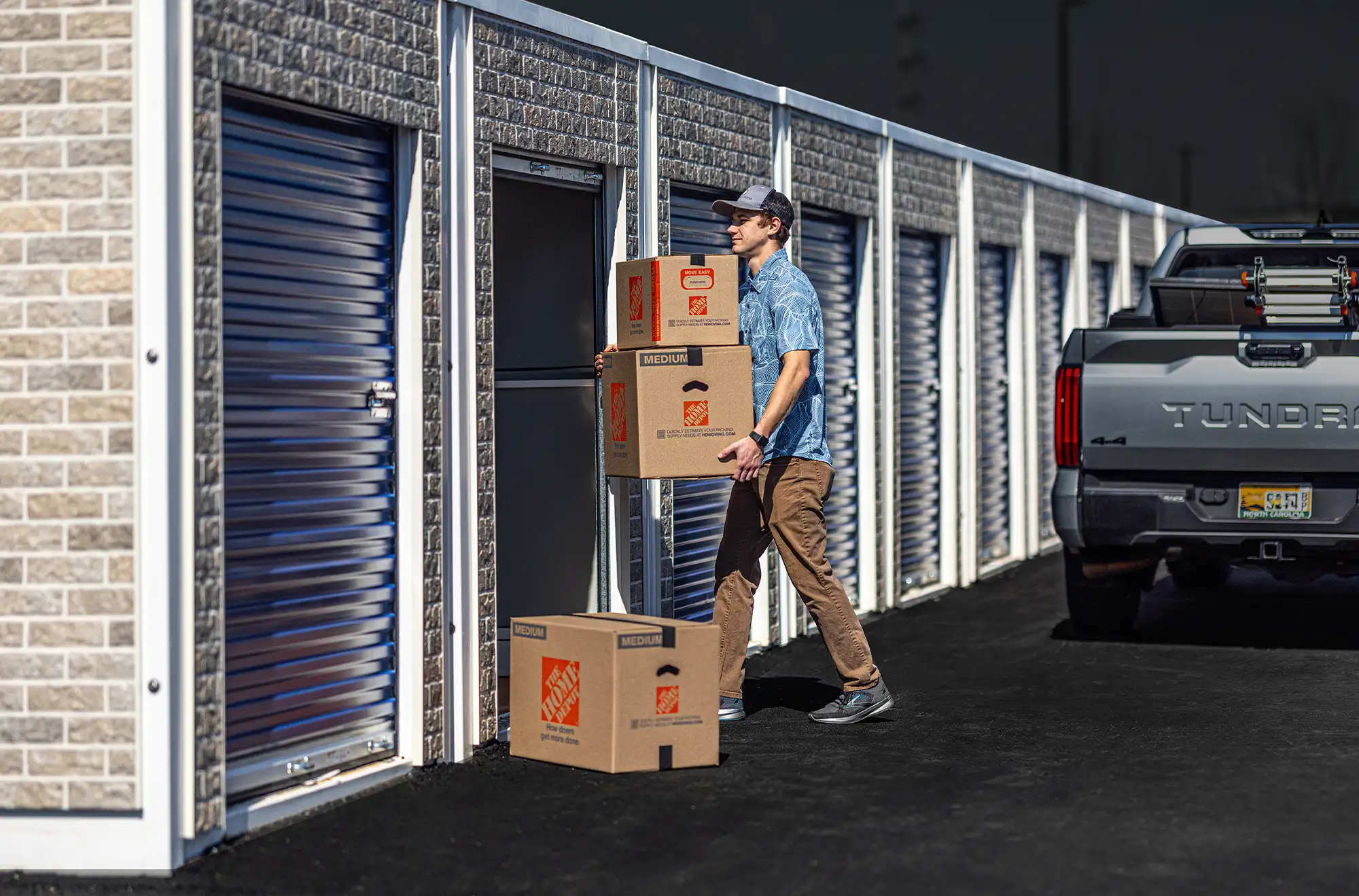 a man in carries Home Depot boxes from his truck into an outdoor storage unit