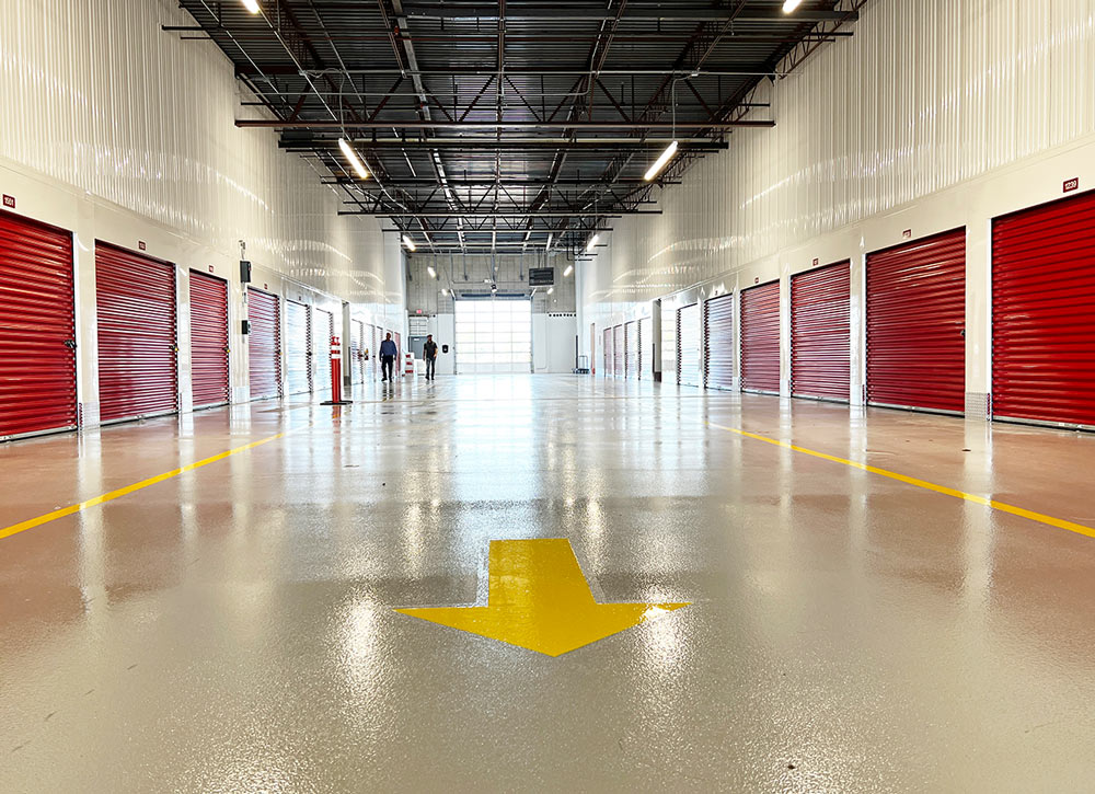 center view down a large drive in storage garage lined with deep red roll-up unit doors