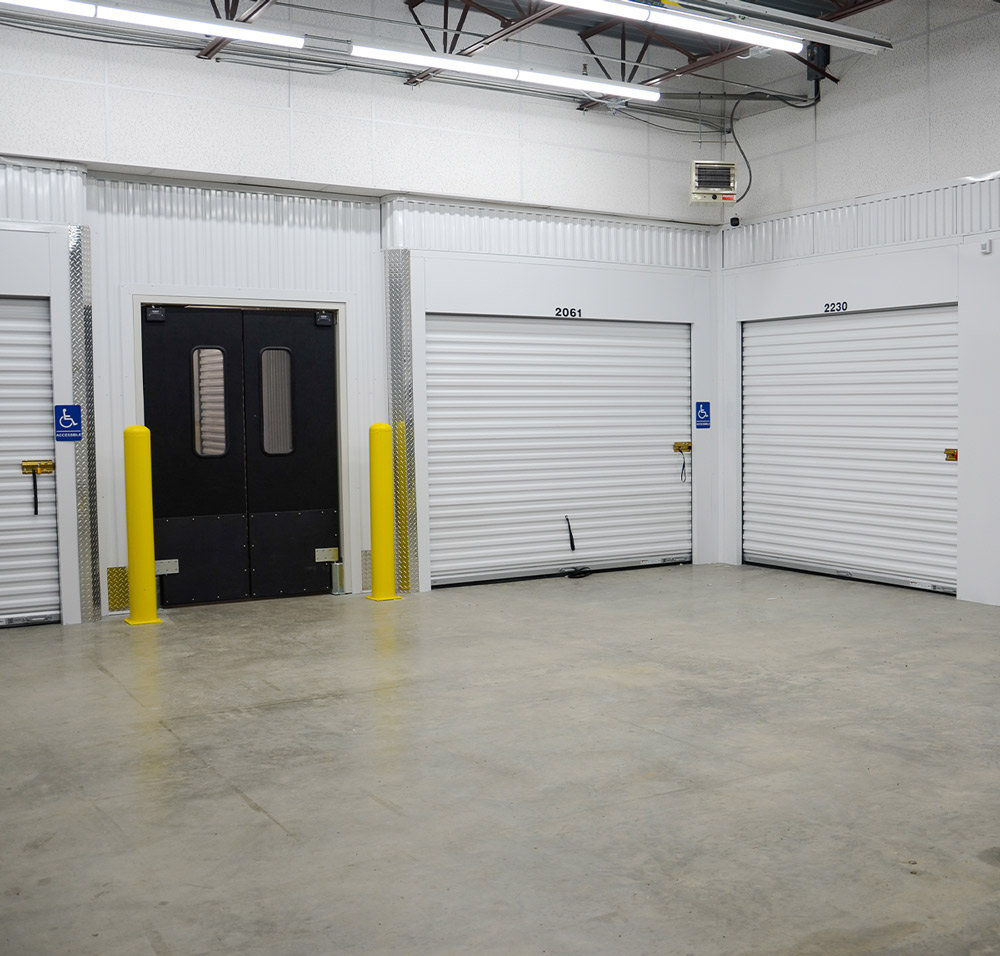 the corner of a storage facility garage with units along the walls and a wide swinging doorway to a corridor beyond