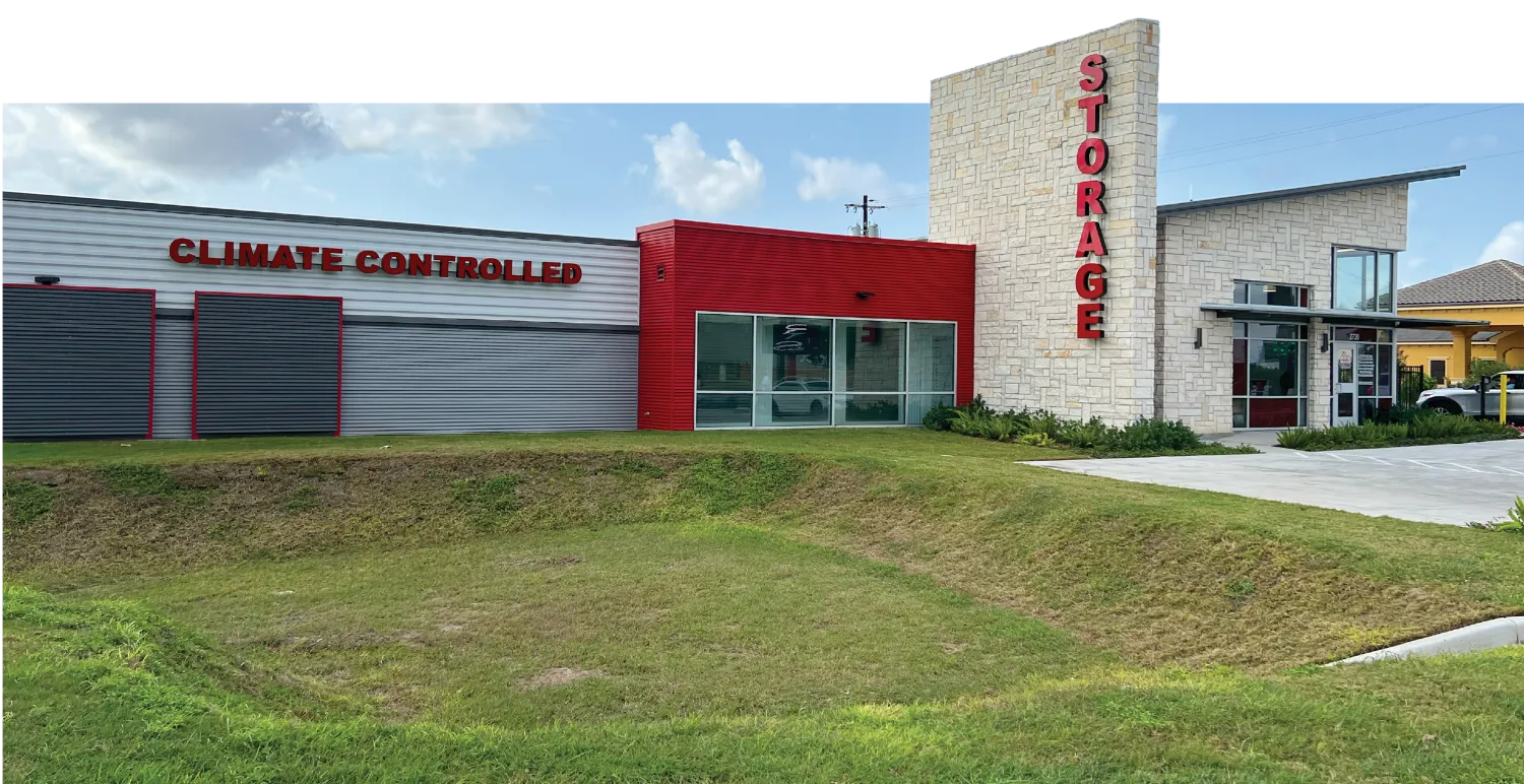 A modern storage facility with a climate-controlled section and a main building with a stone facade labeled 'STORAGE'. The facility is surrounded by well-manicured grass and includes a parking area in front.