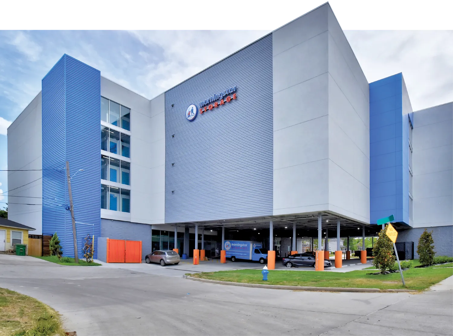 A modern multi-story storage facility with a large blue and gray exterior, labeled 'Morningstar Storage'. Vehicles are parked under the building's overhang near the entrance.