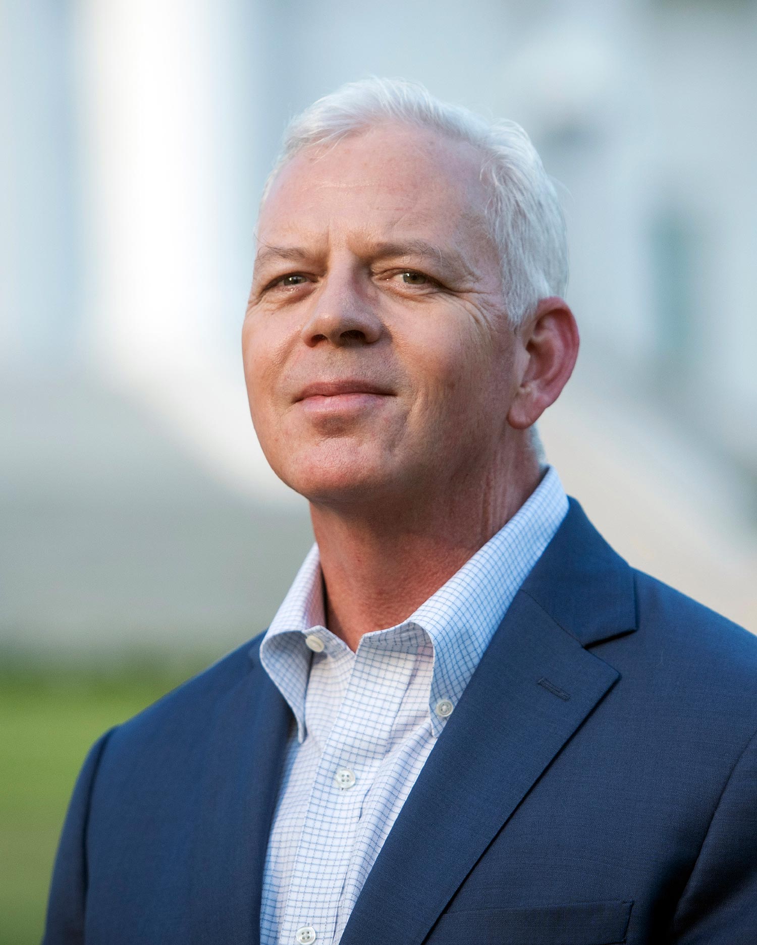 Tim Dietz smiling with white and black grid button up under a navy suit jacket