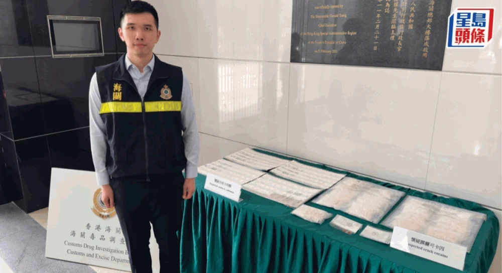 A customs officer stands beside a table covered with seized drugs, displayed in clear plastic bags, as part of a press conference.