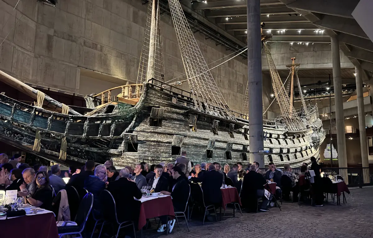 Portrait orientation indoor photograph view of the public enjoying dinner at Vasa Museum as behind them is a big pirate ship on display for everyone to look at