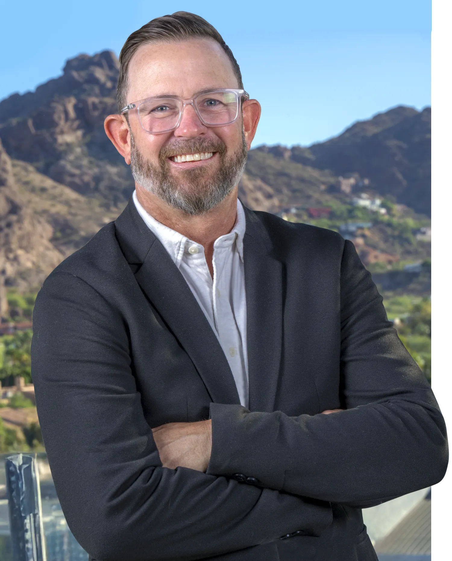 Dave King smiling in suit and clear prescription glasses while arms are crossed with a mountainous landscape behind him