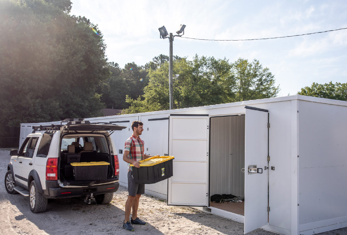 man holding bin of belongings standing in front of open storage unit