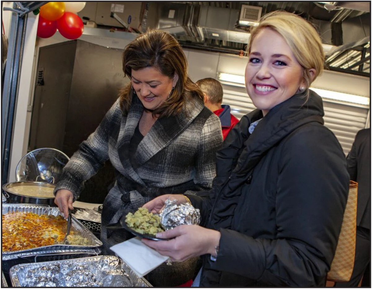 Two women smiling and grabbing food from serving trays