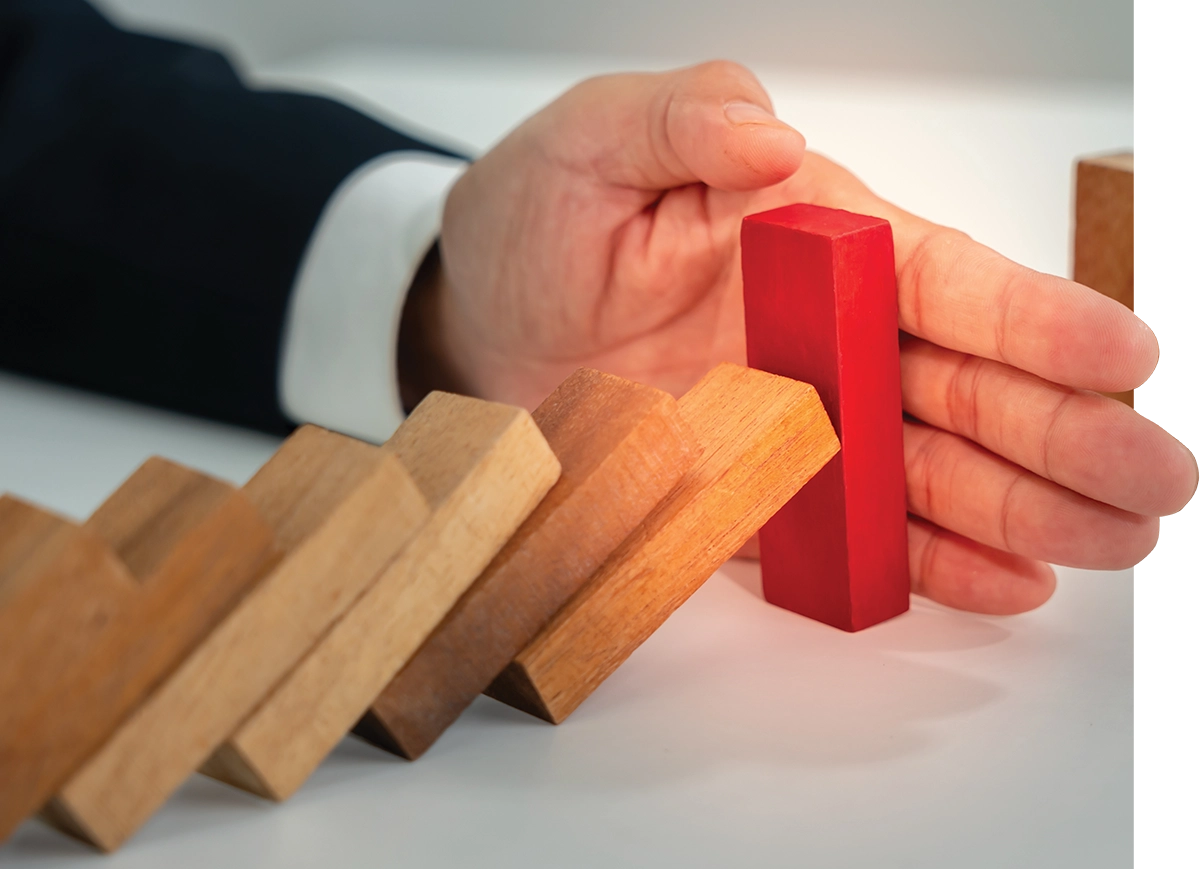 A hand in a suit stops fallen wooden dominoes with a red block.