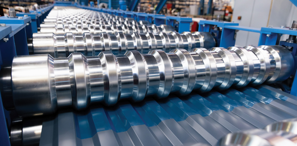 Close-up of large, polished steel rollers shaping blue corrugated metal on a factory production line.