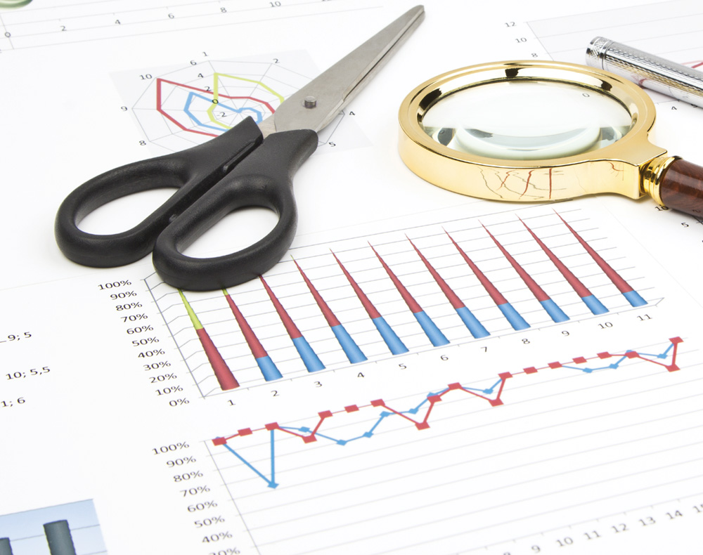 Office items on a desktop with charts, including scissors, a magnifying glass, and a pen.