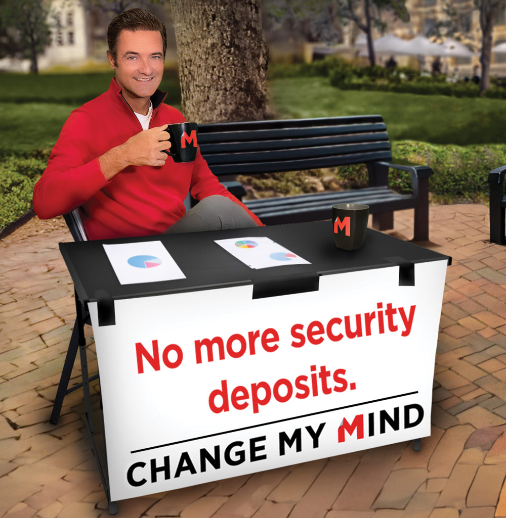 A man in a red sweater holds a mug at a table with charts and a sign that reads "No more security deposits. Change My Mind."