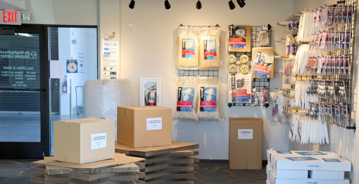 An interior shot of a storage facility office or shop area, featuring cardboard boxes stacked on the left, some with labels.