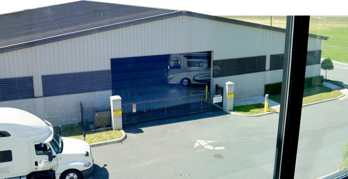 An industrial building with an open door revealing an RV inside, seen from above with a white semi-truck in the foreground.