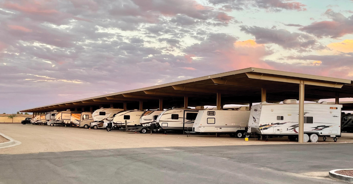 RVs parked under a large metal canopy at sunset or sunrise, with a colorful sky.
