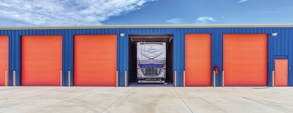 A row of orange roll-up storage unit doors with an open door revealing an RV.