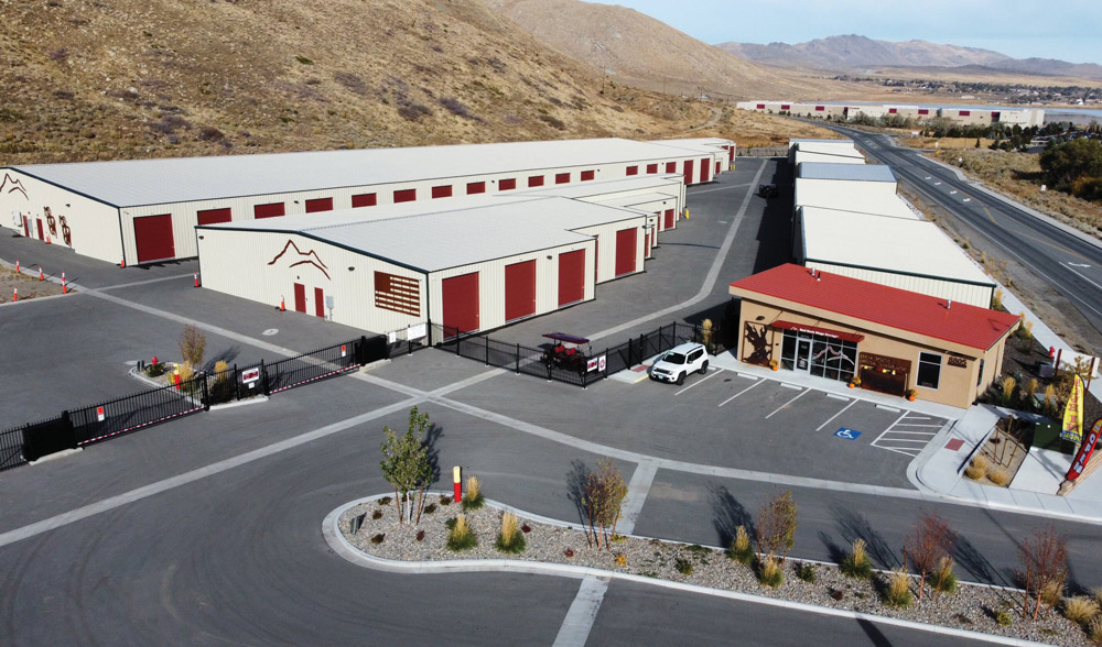 Aerial view of a storage facility with beige buildings and red roofs, set in a hilly, semi-arid landscape.