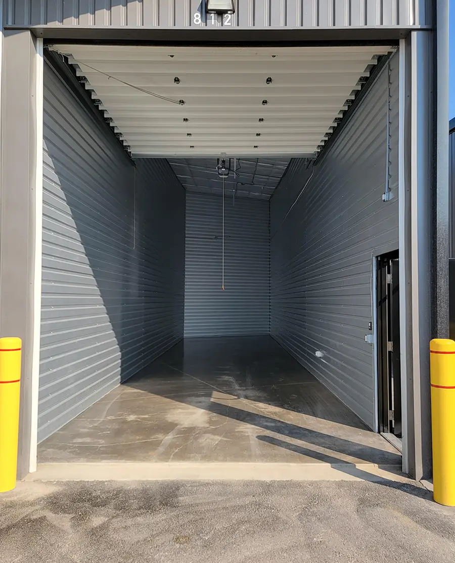 Wide shot inside an empty self-storage unit at Missoula Storage City, featuring a high ceiling, concrete floor, and roll-up door.