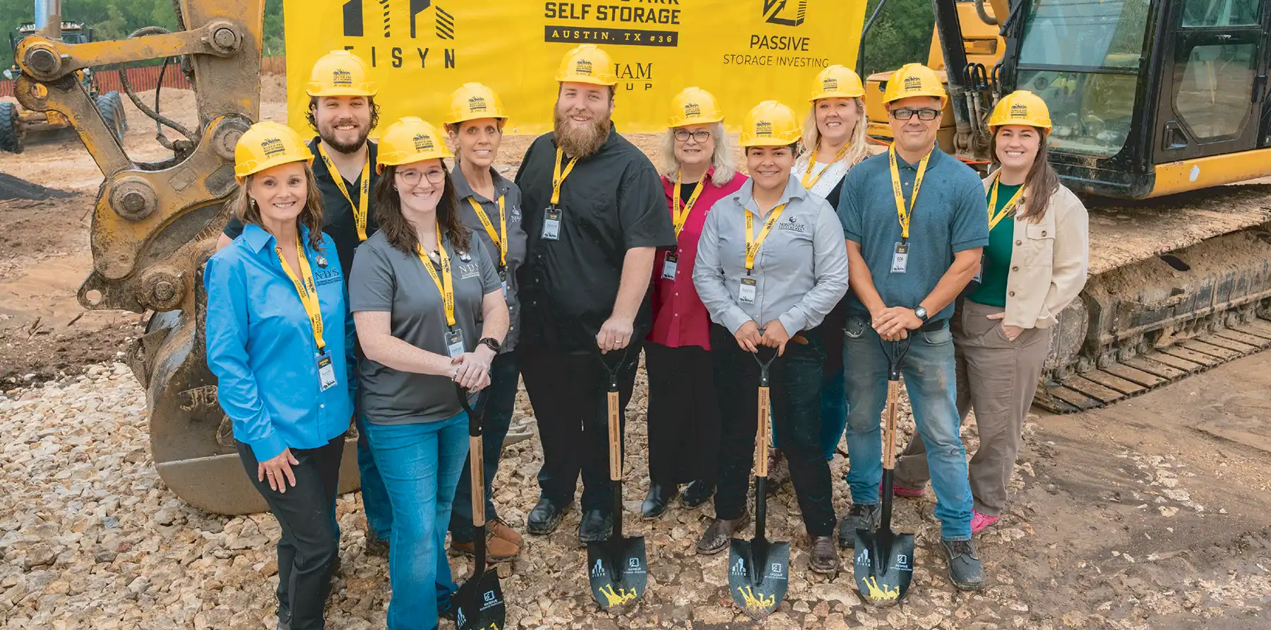 A group of people in construction helmets holding shovels at a construction site.