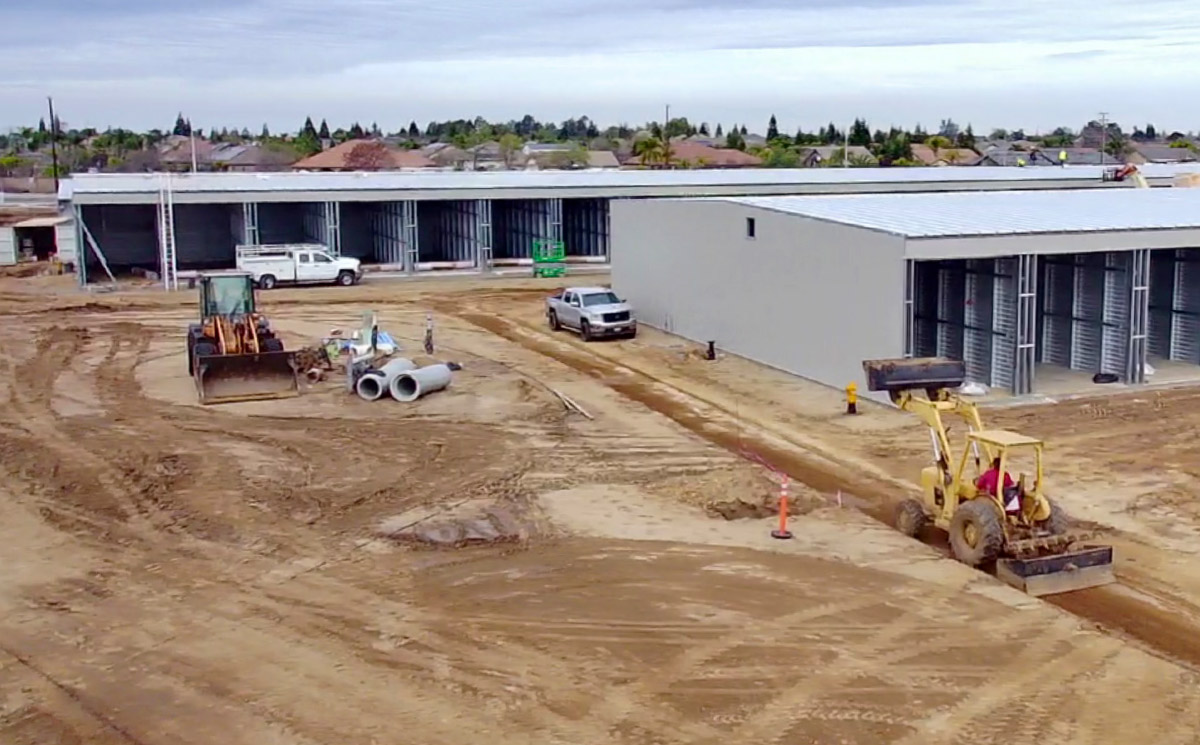 Aerial view of a self-storage facility construction site with a large, dirt lot in the foreground. 