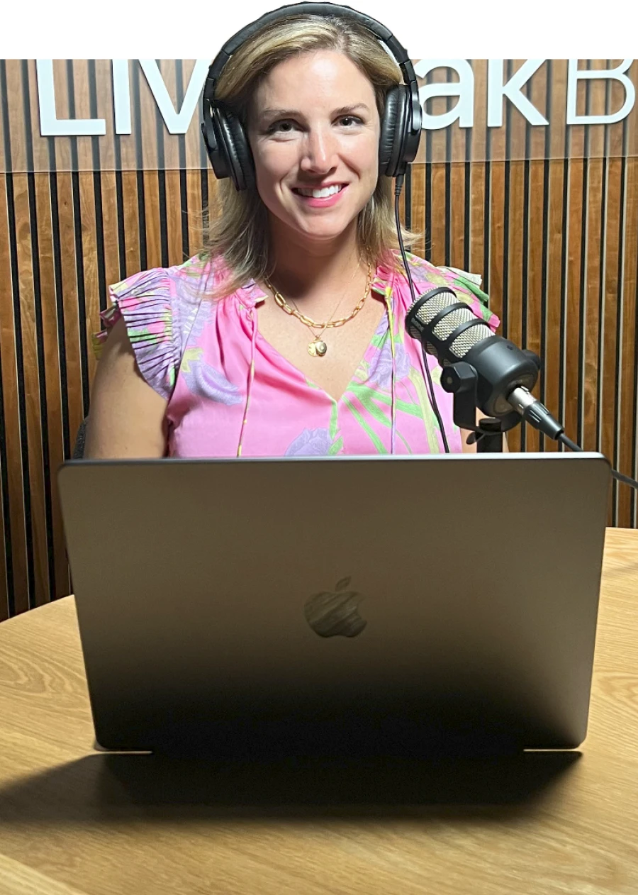 Anna Taylor wearing headphones and seated in front of a mic and laptop, recording a podcast