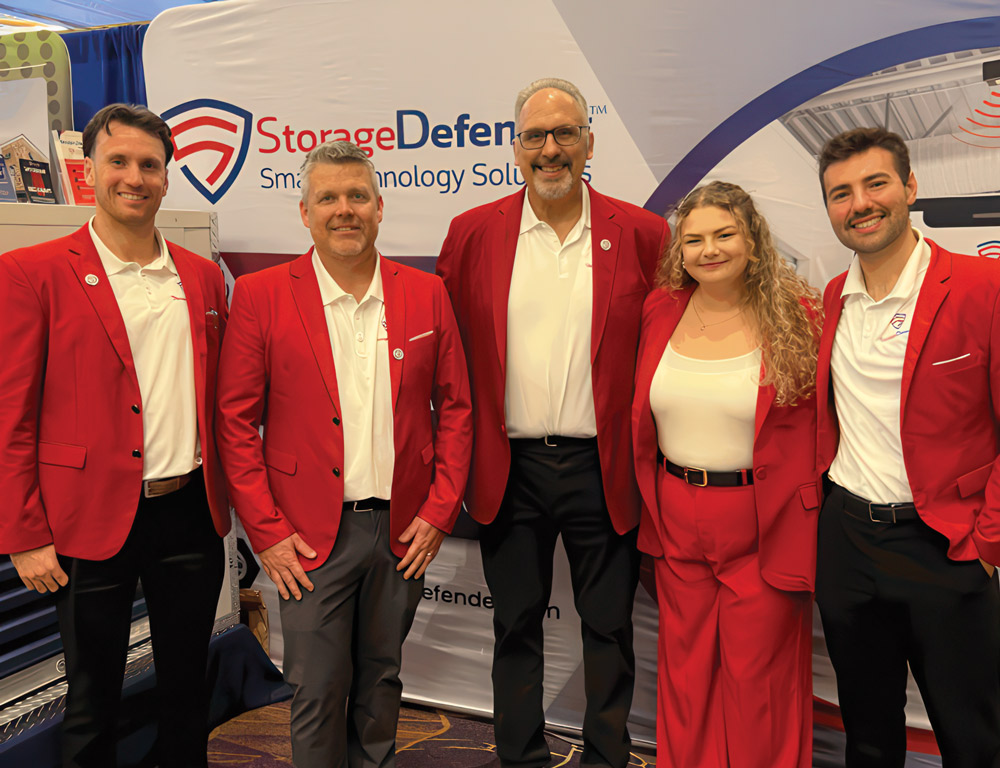 Five StorageDefender team members in red blazers and white shirts posing in front of a company booth.