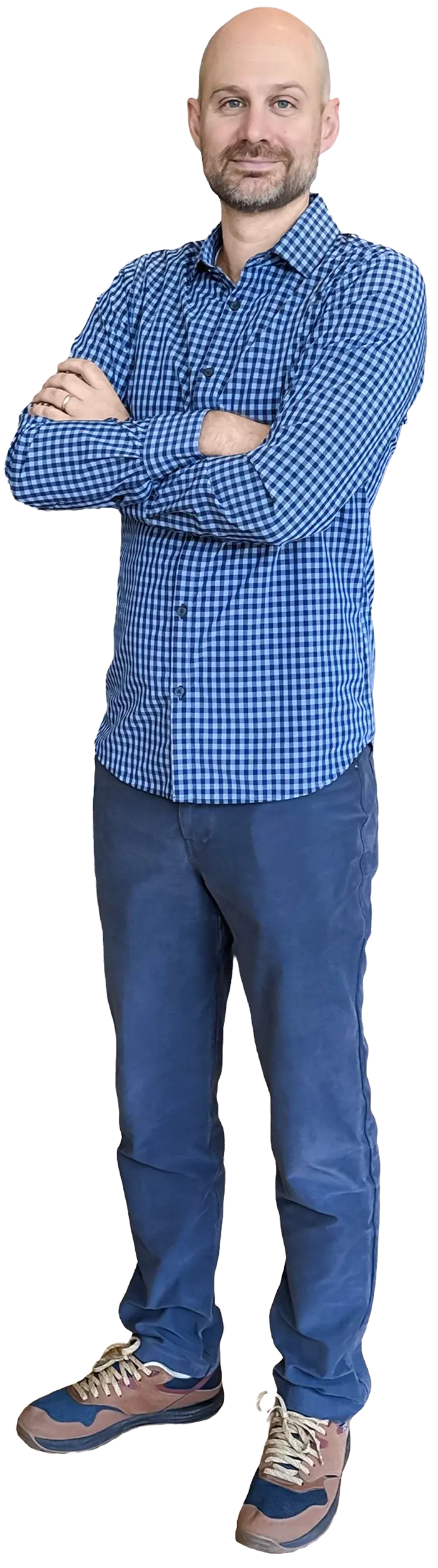 Full-length body portrait photograph of Mitch Briggs, a bald man with a beard, standing with his arms crossed smiling faintly; He's wearing a long-sleeved blue checkered button-up dress shirt, dark blue pants, and blue/brown athletic shoes