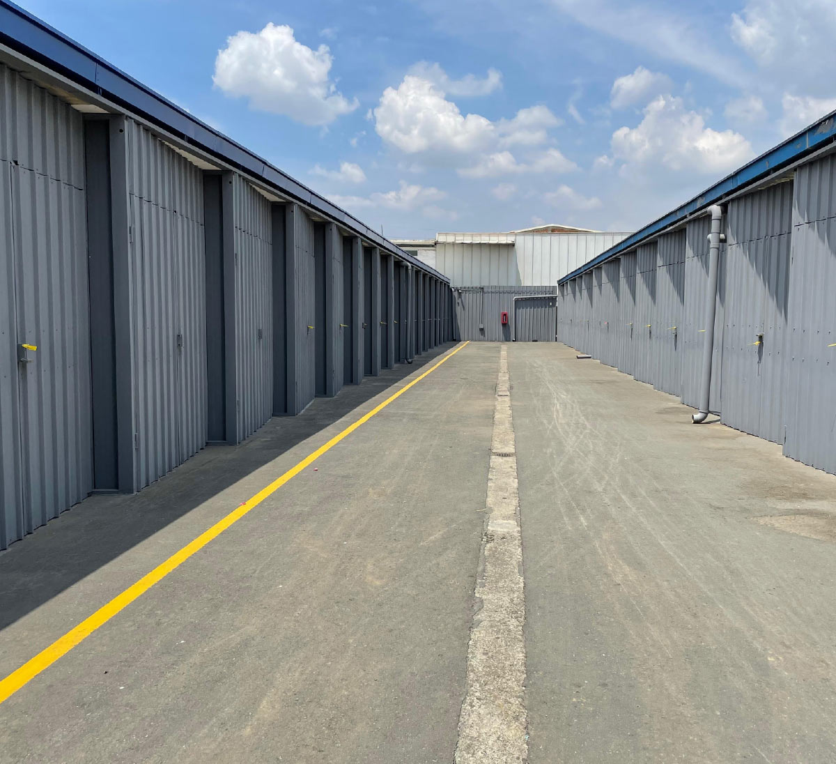 Wide outdoor aisle between two rows of gray self-storage units or warehouses.