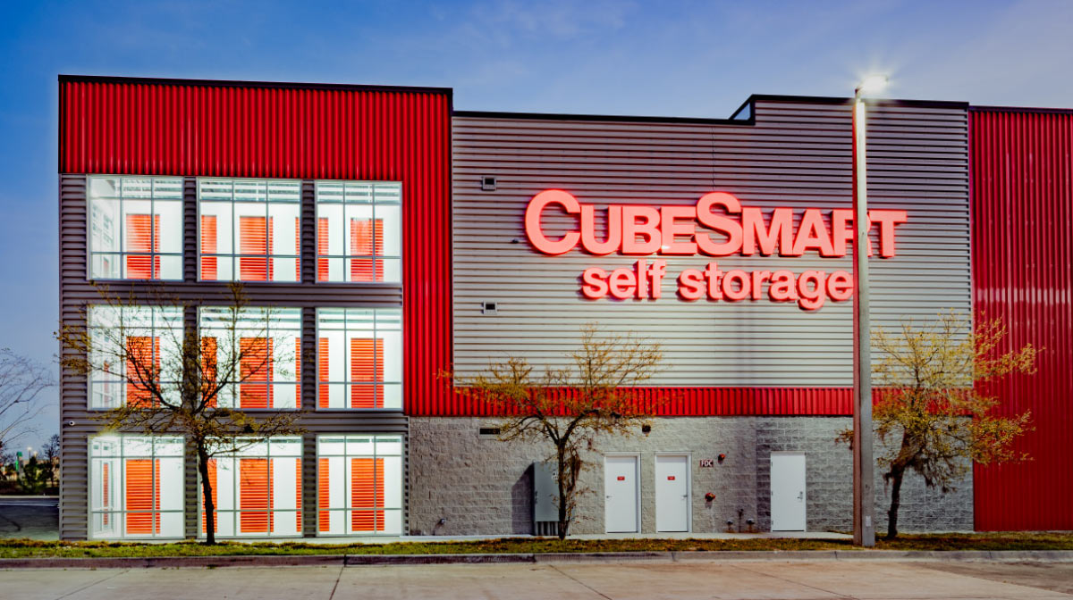 Exterior evening photo of a modern CubeSmart Self Storage facility with glowing red neon signage and large, illuminated windows.