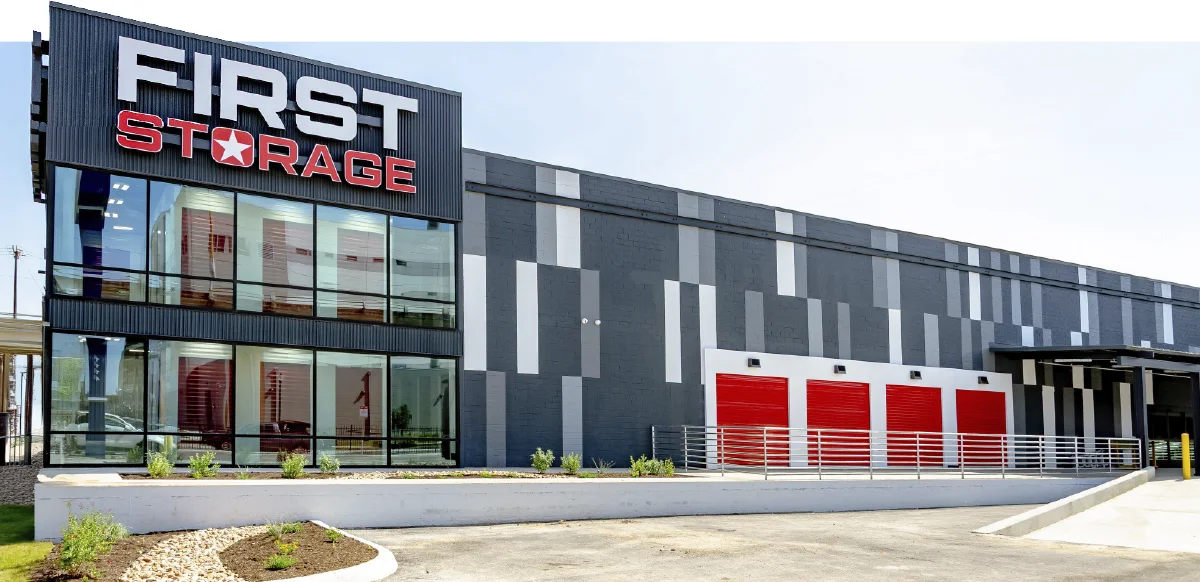 Modern First Storage facility building featuring a glass facade, gray and white exterior, and bright red drive-up storage unit doors.