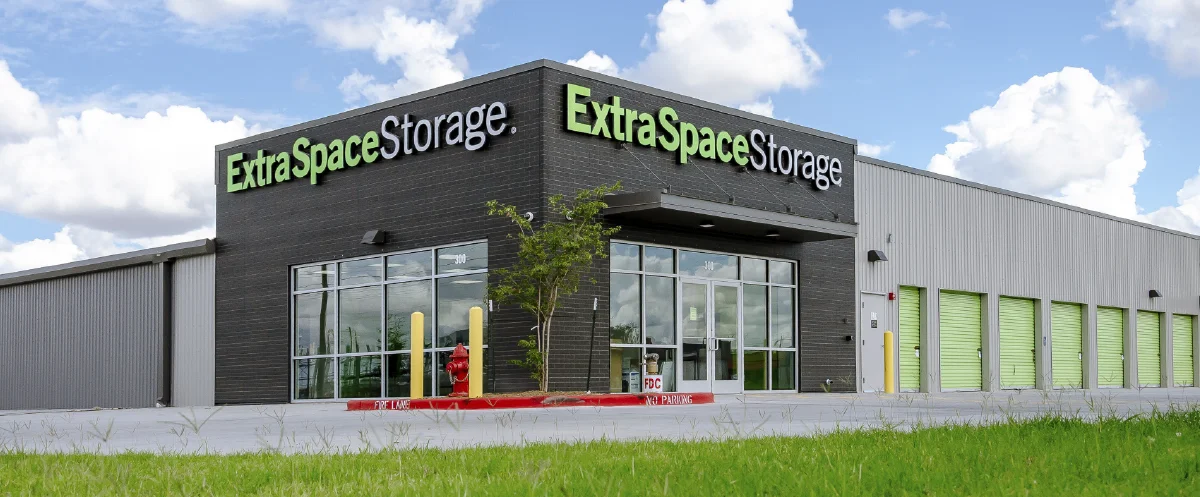 Exterior view of a modern Extra Space Storage facility with a dark gray office facade and bright green storage unit doors.