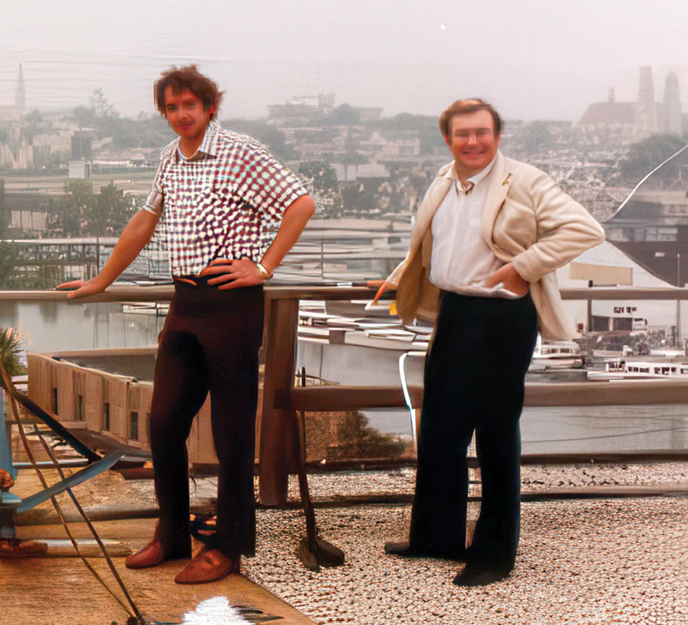 Two men in retro clothing pose on a building rooftop against a hazy city backdrop during the company's early years.
