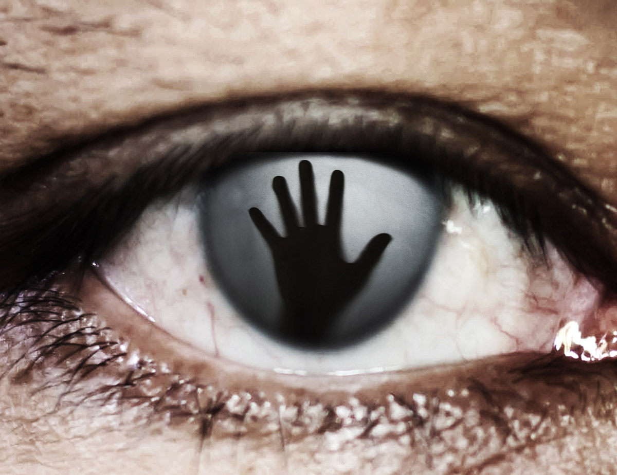 Close-up of an eye with the dark silhouette of a hand pressed against the pupil.
